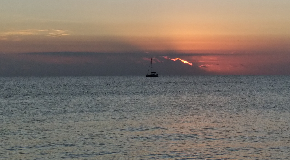 Sunrise with clouds, boat, water, sun and departing darkness